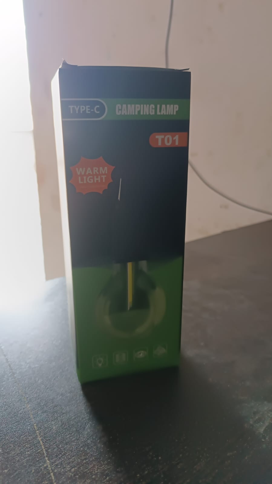 The green and black packaging for a portable LED tent light, labeled "TYPE-C CAMPING LAMP T01" and "WARM LIGHT," stands on a