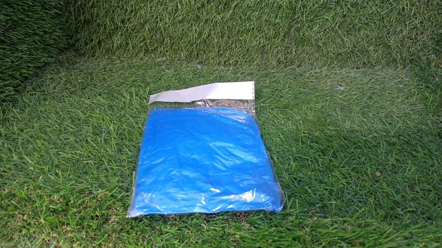 A small, clear plastic package containing a folded blue poncho rests on a vibrant green grass lawn.