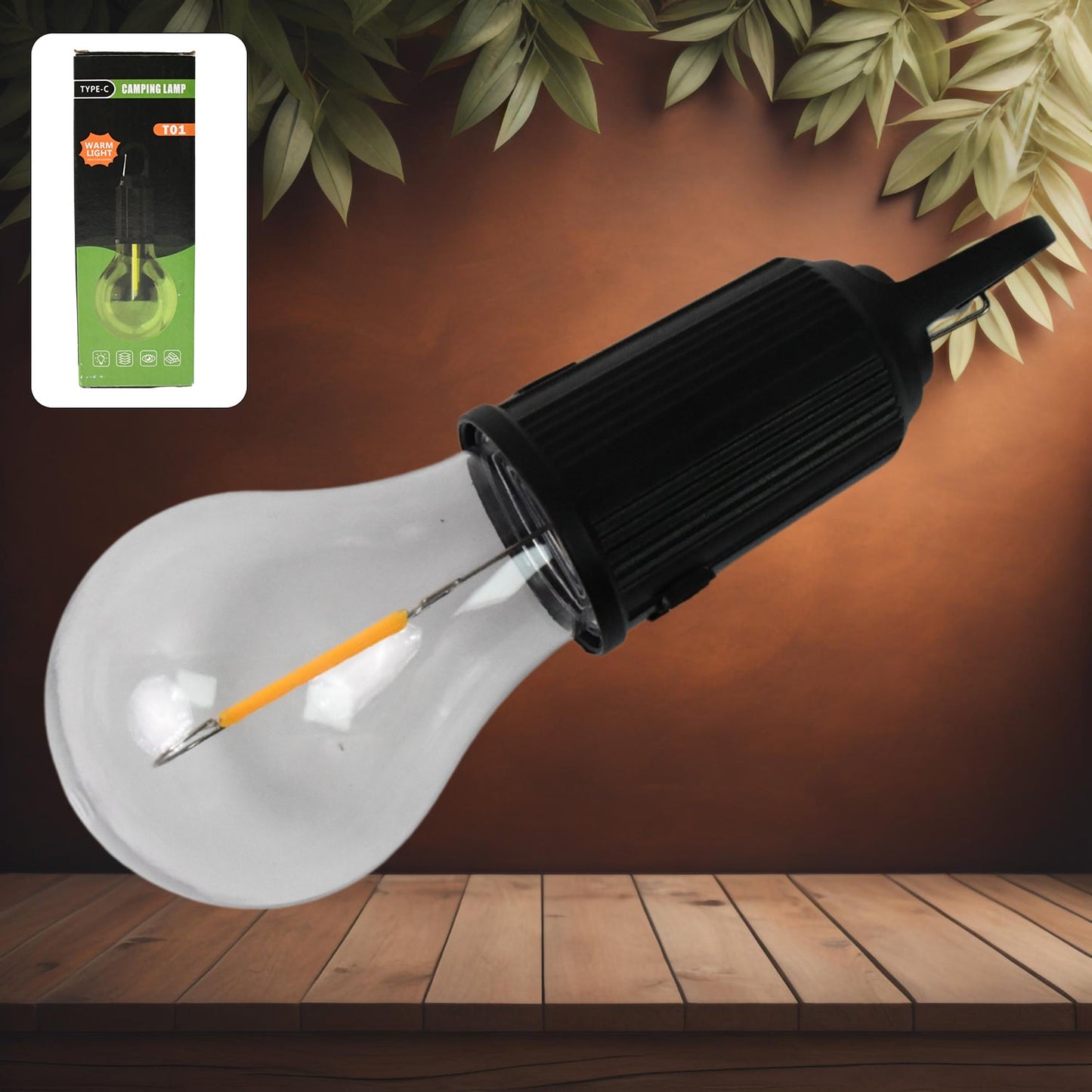 A black and clear portable LED tent light with an orange filament lies diagonally on a wooden surface, with its green and
