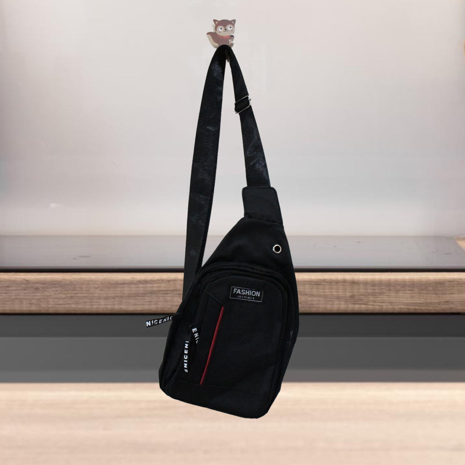 A black sling bag with a red stripe and 'FASHION' label hangs from a small owl hook on a wall.