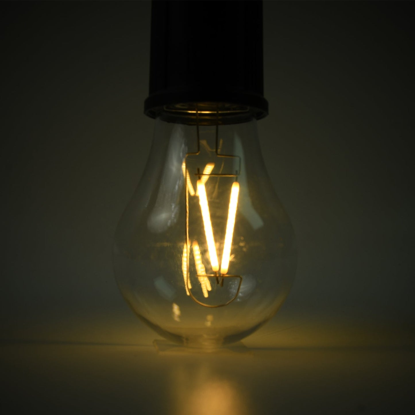 A close-up of the clear bulb of a portable LED tent light shows the glowing orange filament against a dark background.